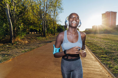 Happy sportswoman listening to music on headphones and jogging in park