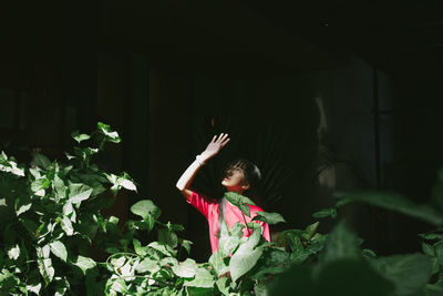 Woman covering face while standing amidst plants