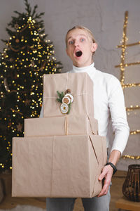 Funny man in front of christmas tree ready for celebration with big giant gifts, emotional person