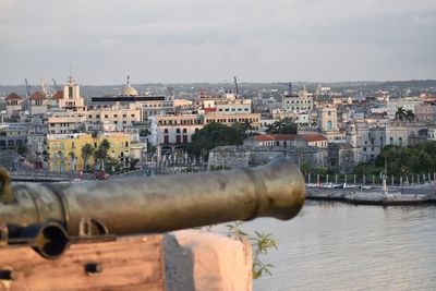 Cityscape by river against sky in city