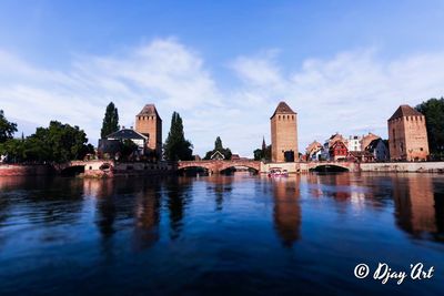 View of buildings by river against cloudy sky