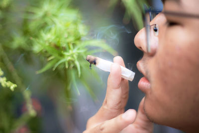 Close-up of boy smoking joint while sitting outdoors
