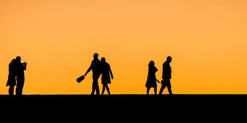Silhouette people walking against clear sky during sunset