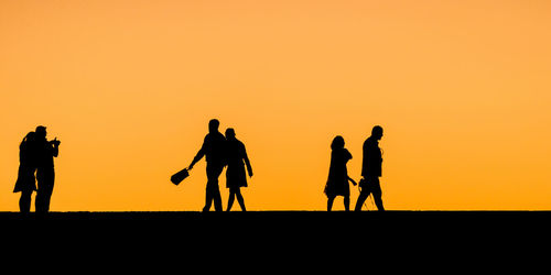 Silhouette people against orange sky