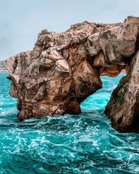 Rock formation by sea against clear blue sky