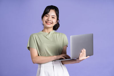 Portrait of young woman using laptop while standing against blue background