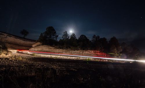 Light trails on road by field at night