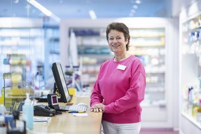 Happy pharmacist leaning on desk