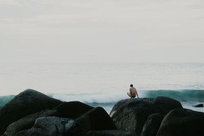 Man sitting on rock looking at sea against sky