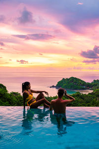 Rear view of woman swimming in sea against sky during sunset