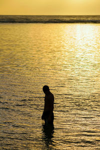 Silhouette man in sea against sky during sunset