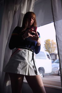 Young woman using mobile phone while standing in car