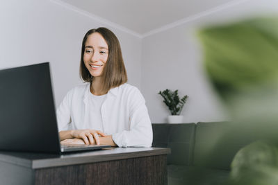Smiling young woman using laptop on table at home