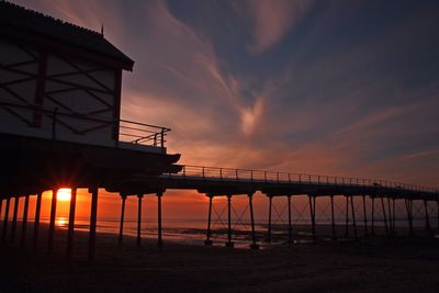 Silhouette built structure on beach against sky during sunset
