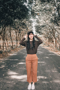 Smiling young woman looking away while standing on road amidst trees in forest