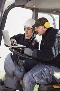 Construction workers using laptop in excavator