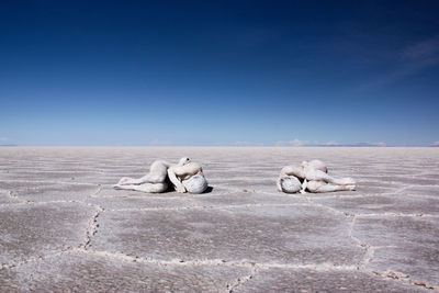 High angle view of sensuous naked man and woman covered with powder lying on barren land against clear sky