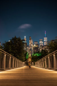 Man by illuminated bridge and buildings against sky at night