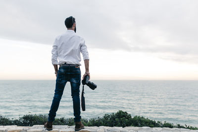 Rear view of man standing on retaining wall against sea