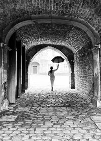 Full length rear view of woman with umbrella walking in tunnel