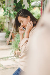 Woman looking down while talking on mobile phone against trees