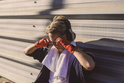 Boy with headphones rubbing eyes while sitting by wall