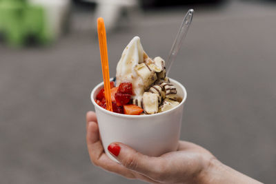 Close-up of female hand holding a cup of frozen joghurt with various toppings