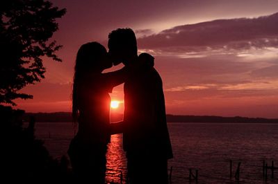 Man and woman kissing while standing by rappahannock river during sunset