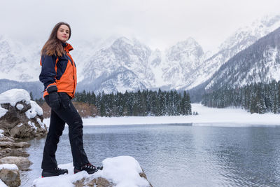 Young woman standing by frozen lake against mountains during winter