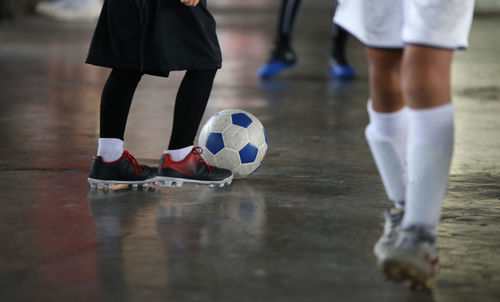 Low section of people playing with soccer ball on floor