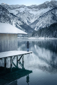 Rear view of person standing by lake during winter