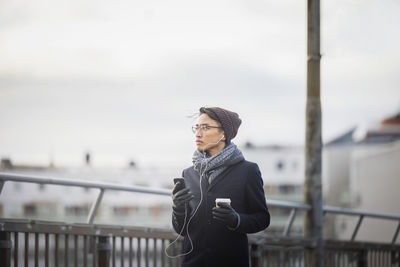 Handsome man with smartphone and paper cup on footbridge