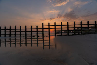 Silhouette wooden posts on beach against sky during sunset