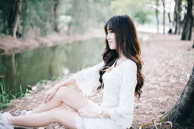 Woman sitting by lake against trees in forest