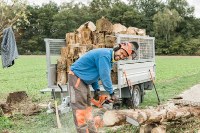 Portrait of smiling worker cutting tree trunk outdoors