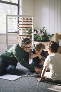 Senior female teacher explaining preschool boys sitting in classroom at preschool