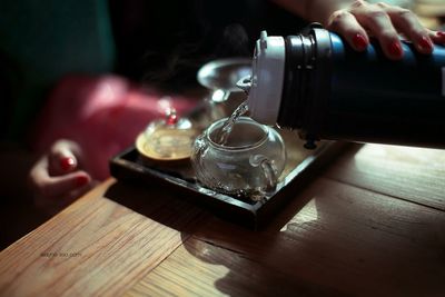 Midsection of woman pouring water in tea cup on table