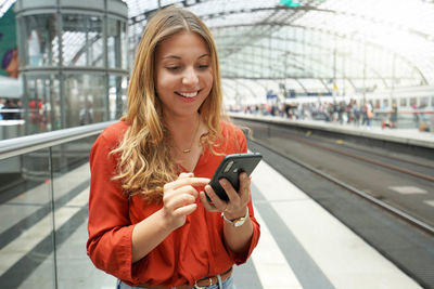 Smiling attractive brazilian traveler passenger buys ticket online with smartphone in train station.