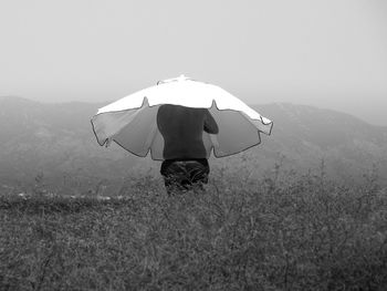 Rear view of shirtless man with beach umbrella standing on field against clear sky