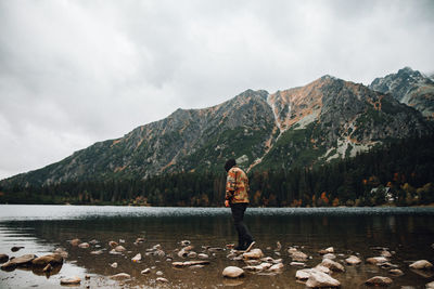 Side view of man standing on rock over lake against mountains