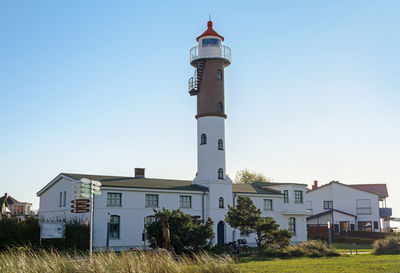 Lighthouse by buildings against clear sky