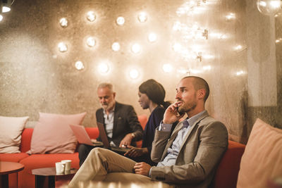 Businessman talking on smart phone while sitting with coworkers in office