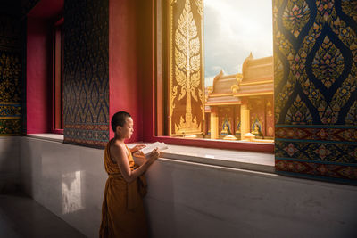 Monk reading book at window in temple