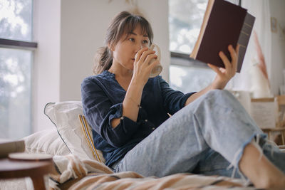 Woman reading book while sitting at home