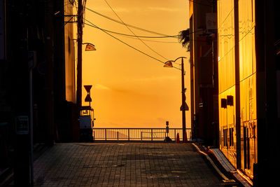 Street amidst silhouette buildings against sky during sunset