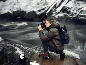 Profile view of man photographing with camera at riverbank during winter