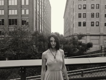 Portrait of young woman standing against buildings in city