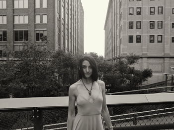 Portrait of young woman standing against building in city