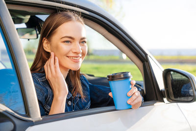 Beautiful young woman traveled on road in car, drinking coffee from disposable