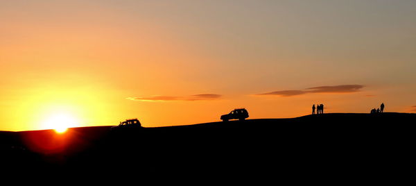 Silhouette people on land against sky during sunset